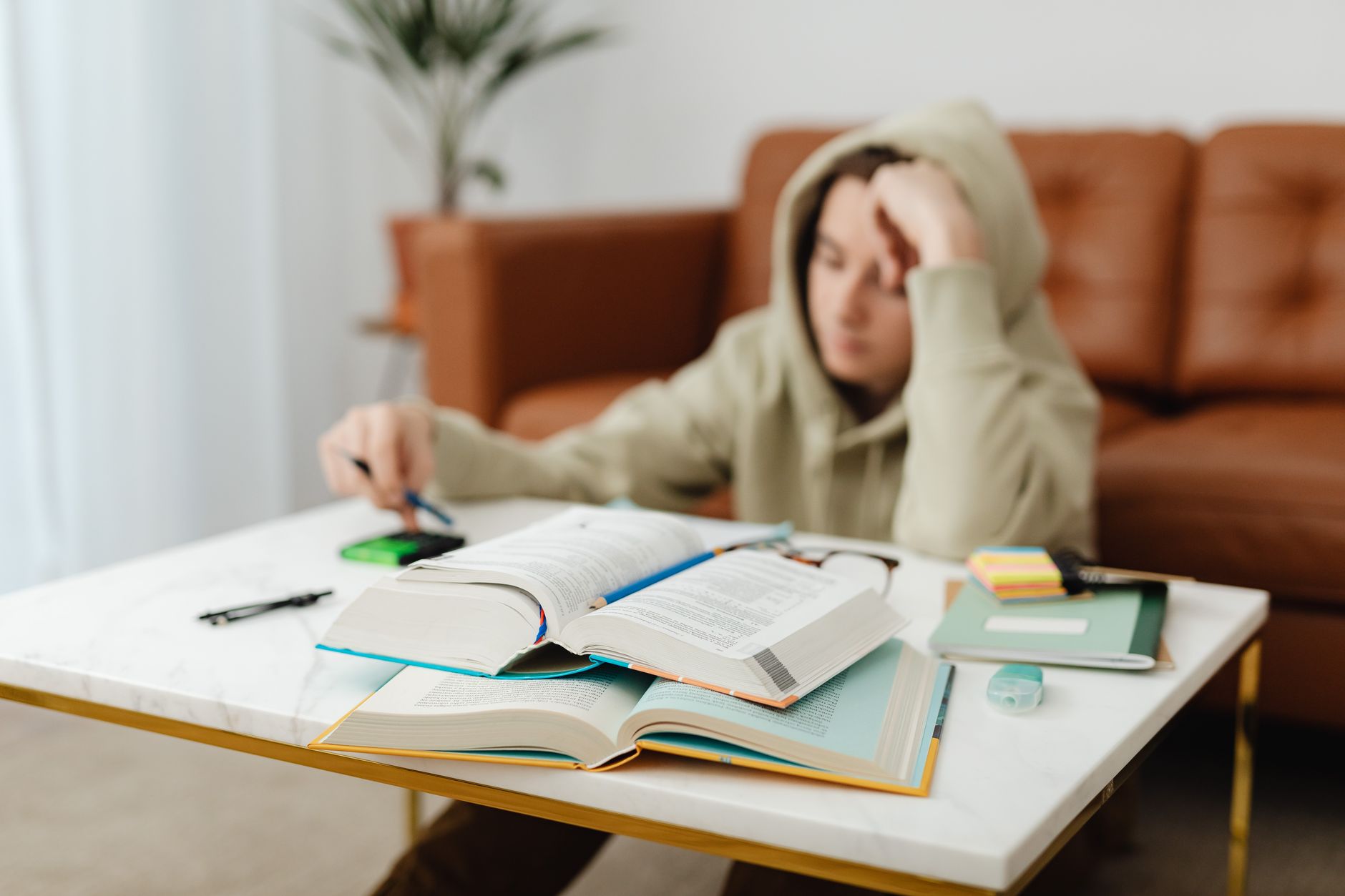 A student studying at a desk covered with open books and notes
